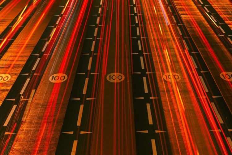 Overhead view of a highway with speed limit signs and red streaks of light from traffic at night